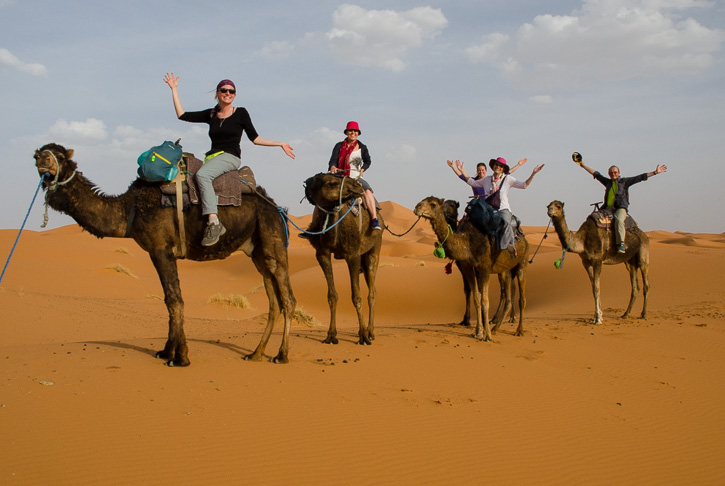 Group image of people riding camels in desert